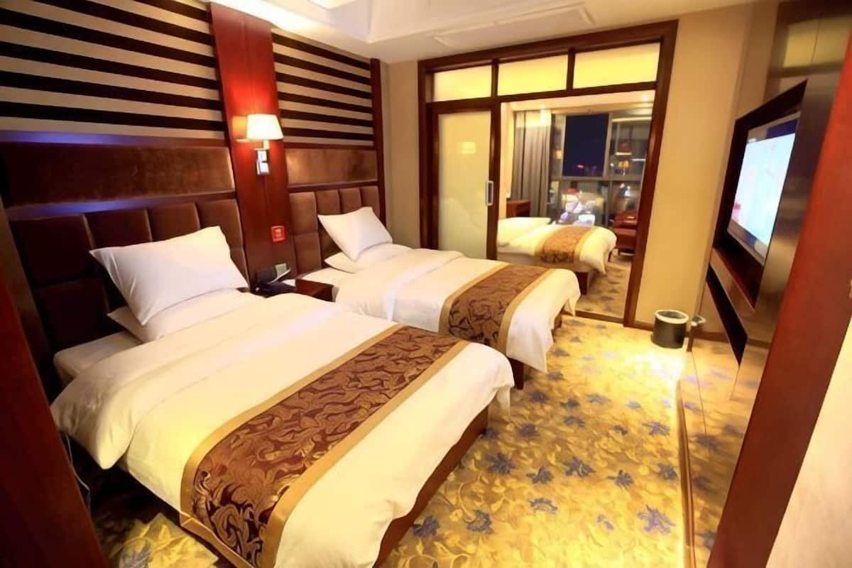 A hotel room with two beds, a television, a nightstand, and a window with a view.