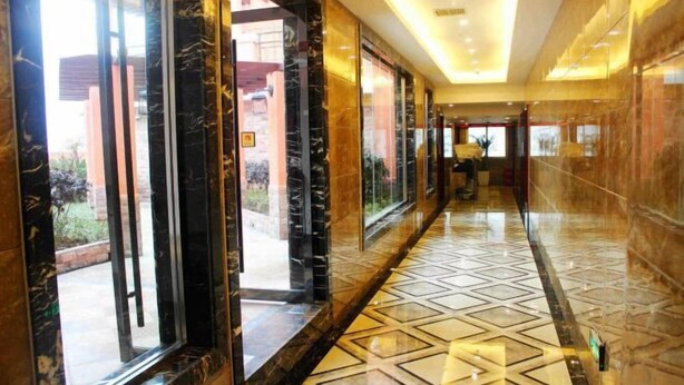 A corridor with marble walls and a patterned floor, leading to a reception area.