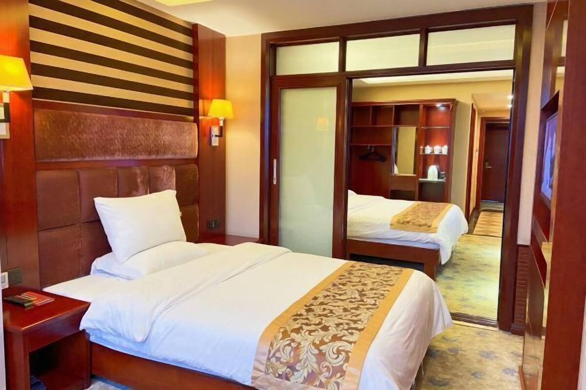 A hotel room with two beds, a wooden headboard, a wardrobe with a mirror, and a bedside table with a lamp.