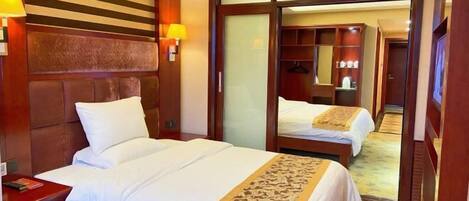 A hotel room with two beds, a wooden headboard, a wardrobe with a mirror, and a bedside table with a lamp.