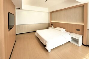 Una habitación de hotel moderna con una cama grande, una mesita de noche, un televisor montado en la pared y un cabecero de madera.