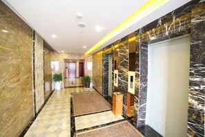 A hotel corridor with marble walls, a checkered floor, and a reception desk.