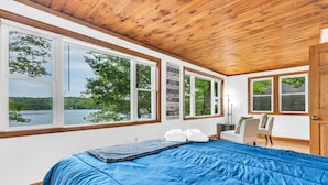 Un dormitorio con una cama grande, varias ventanas y vistas a un lago.