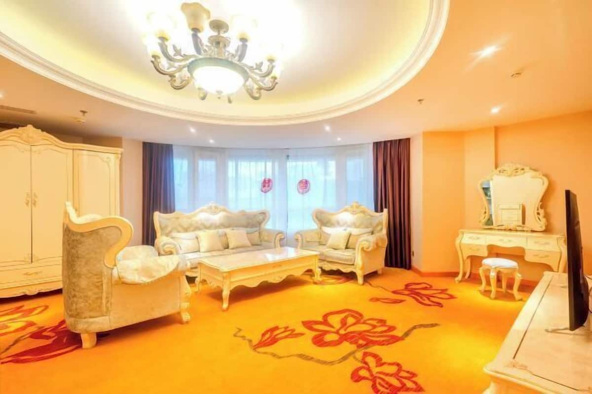 A room with a sofa, armchairs, a coffee table, a TV, a dresser, and a chandelier.