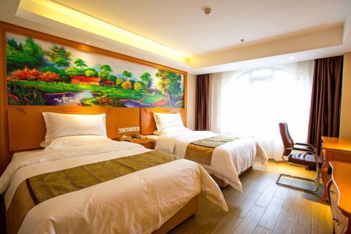 A hotel room with two beds, a desk, a chair, and a large painting on the wall.