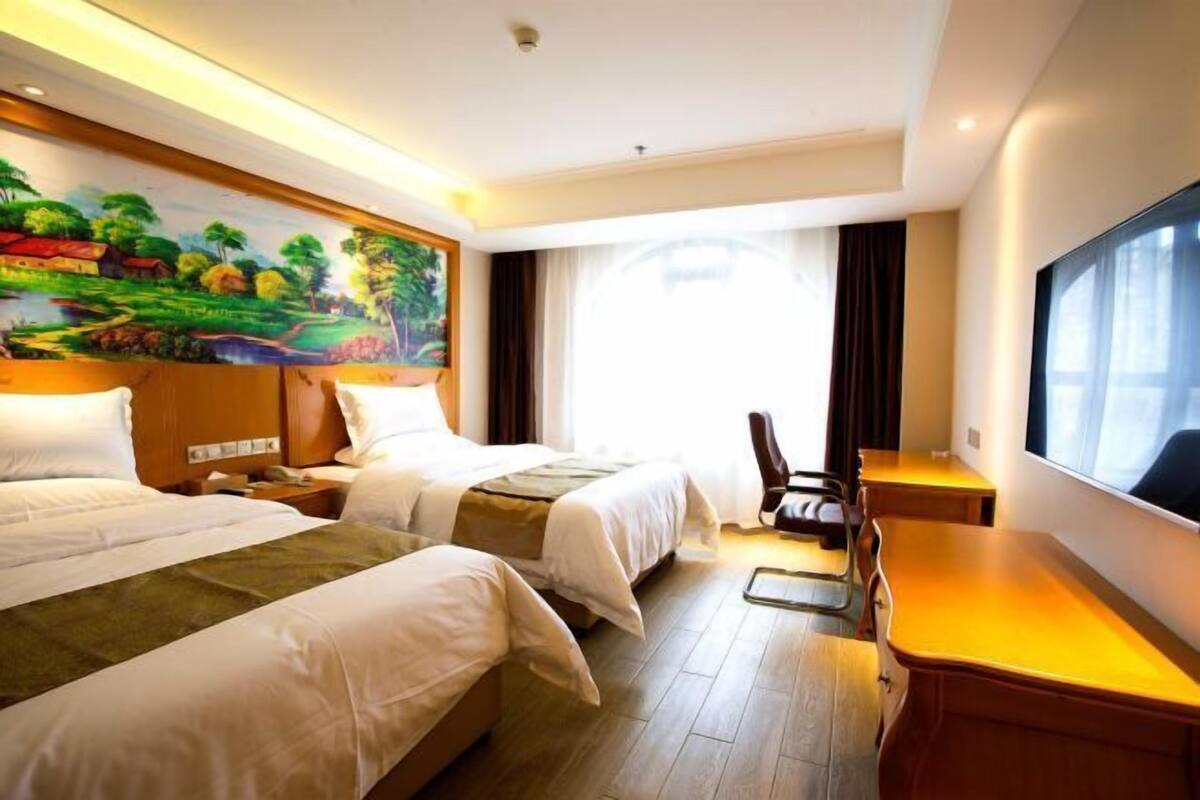 A hotel room with two beds, a desk, a chair, a large window, and a mural on the wall.
