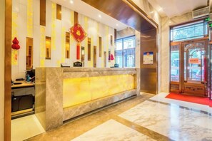 A hotel reception area with a marble reception desk, a red carpet leading to the entrance, and a traditional Chinese decorative element above the desk. - Langman Xicheng Hotel (Harbin)