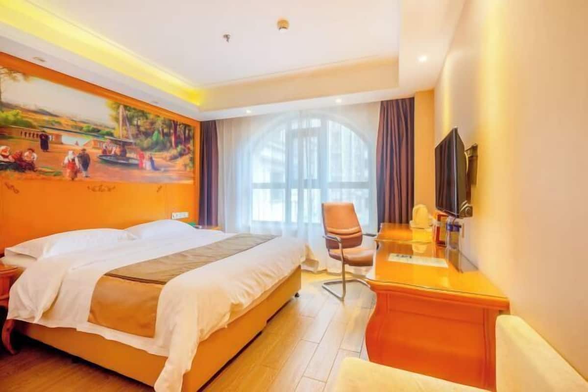 A hotel room with a bed, a desk, a chair, a TV, and a large window with curtains.