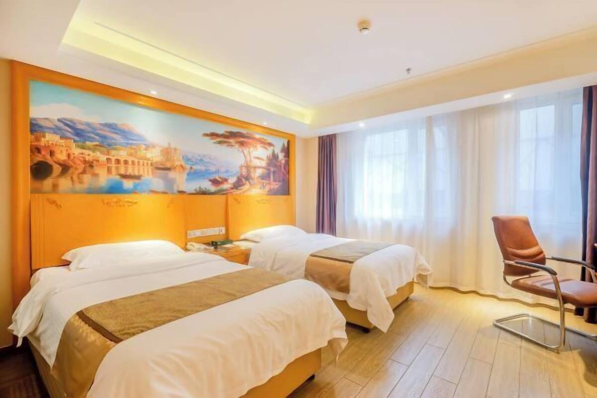 A hotel room with two beds, a painting on the wall, a chair, and a window with curtains.