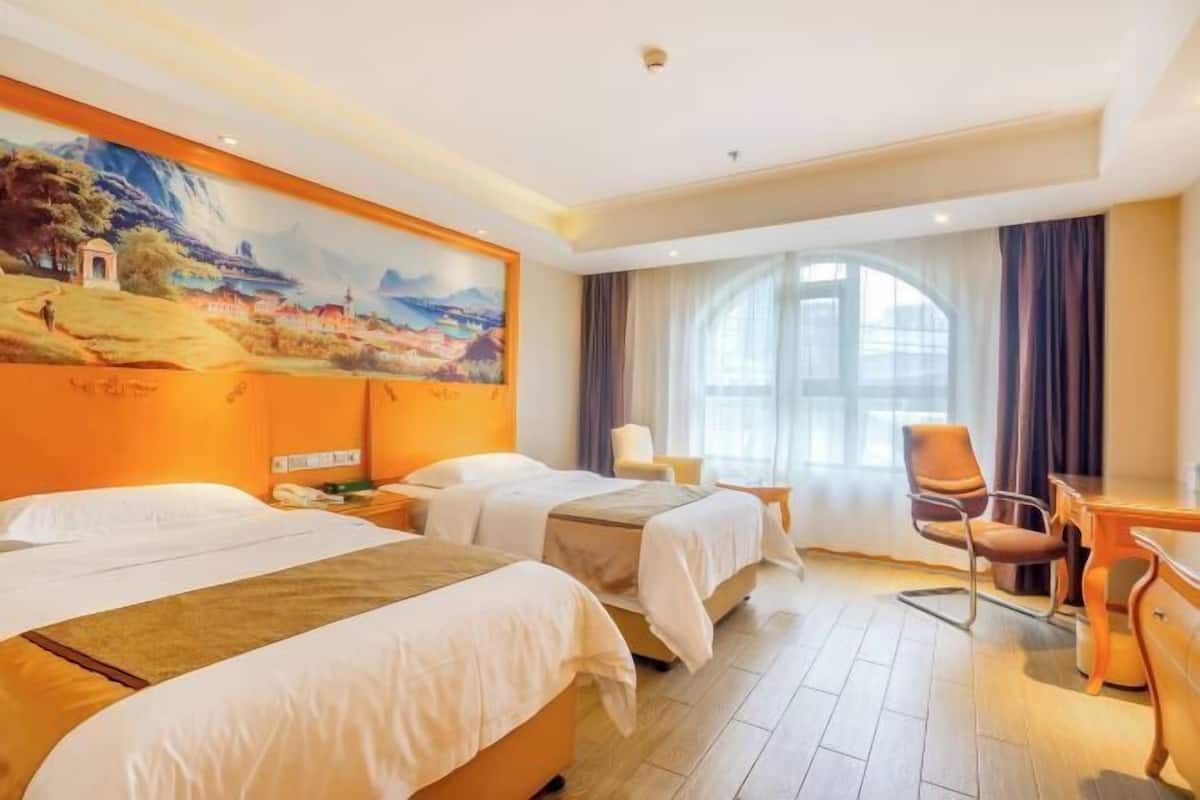 A hotel room with two beds, a desk, a chair, and a large painting on the wall.