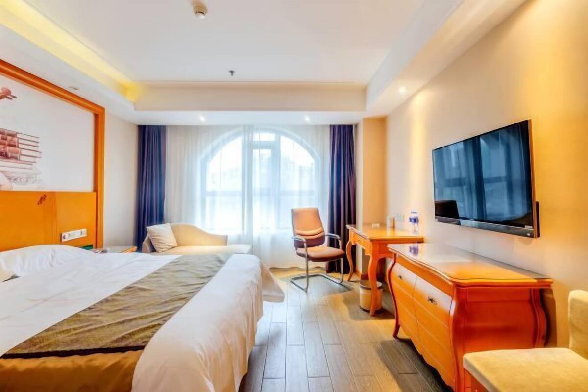 A hotel room with a bed, a desk, a chair, a TV, and a window with curtains.