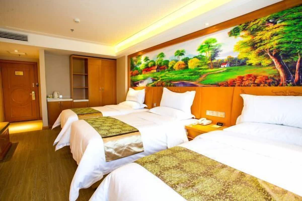 A hotel room with two beds, a painting of a landscape on the wall, and a wooden wardrobe.
