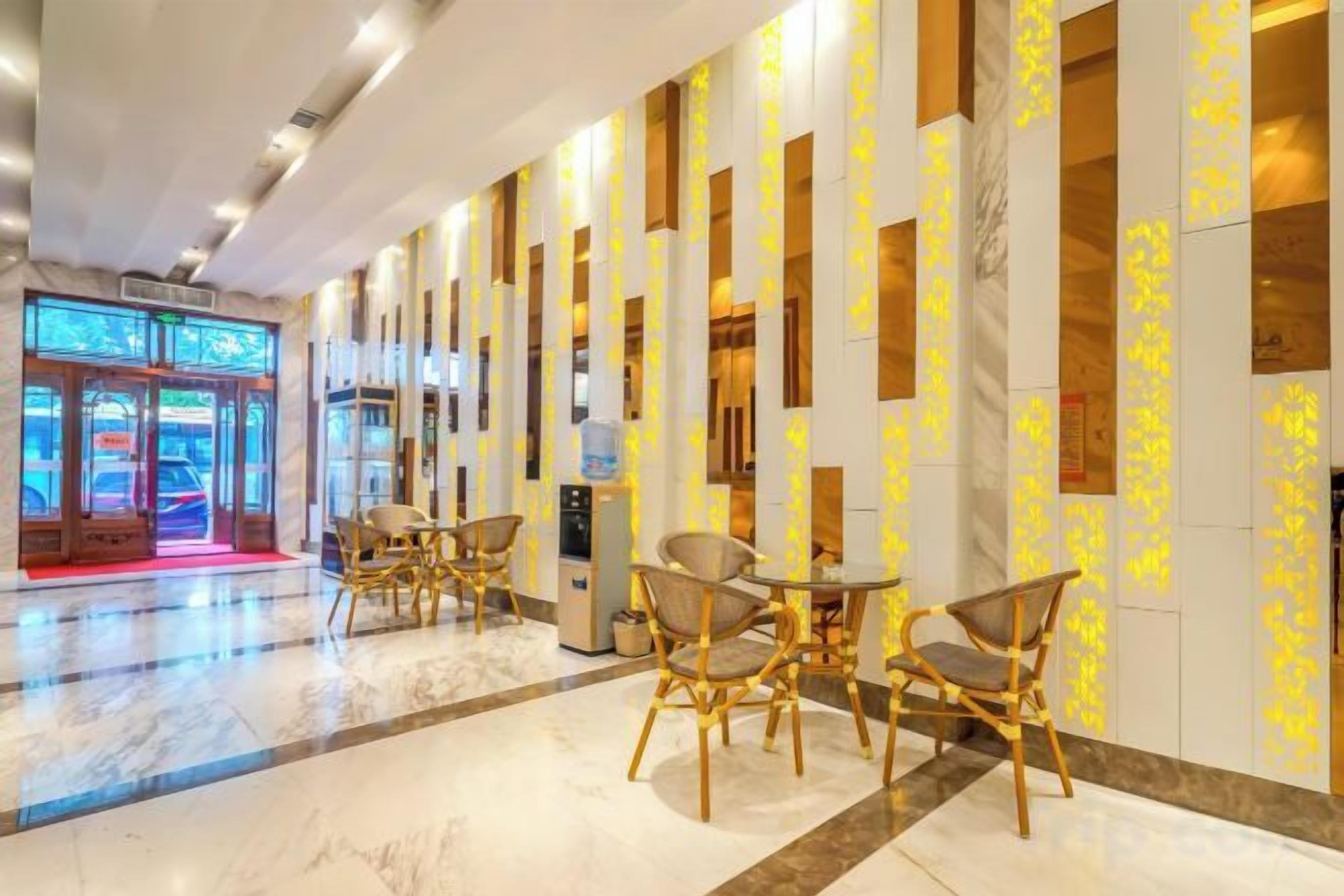 Un vestíbulo de hotel con piso de mármol, zona de estar con sillones y una recepción.