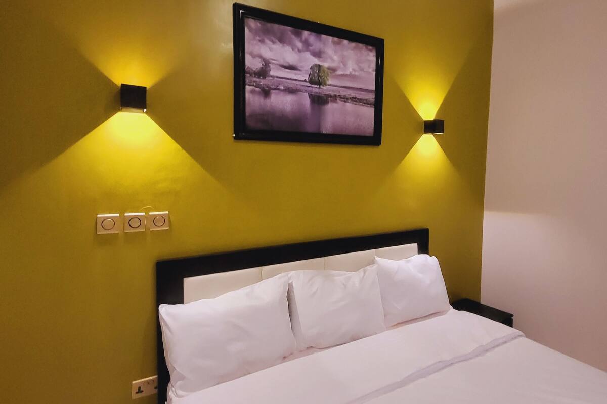 Een hotelkamer met een bed, een airconditioner, een aan de muur hangend schilderij en twee wandlampen.
