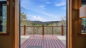 A wooden deck with a railing, a clear sky, and a forested hill in the background.