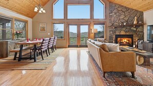 A spacious living area with a stone fireplace, wooden ceiling, and large windows. - Your Mountain Base-Where Trail Ends & Views Begin (Murphy)
