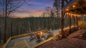 A wooden deck with a fire pit and chairs, surrounded by a forest.