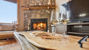 A cozy living room with a stone fireplace, a flat-screen TV, and two wine glasses on a wooden table.