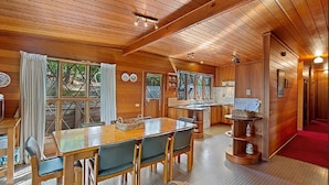 Een houten chalet van binnen, met een eethoek, keuken en een rode gang.