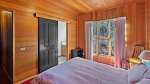 Een kamer met houten lambrisering, een bed, een raam met gordijnen en een deur.