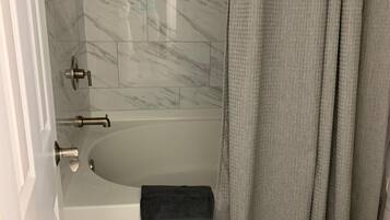 Et badeværelse med et hvidt badekar, en bruseforhæng og toiletartikler på væggen.