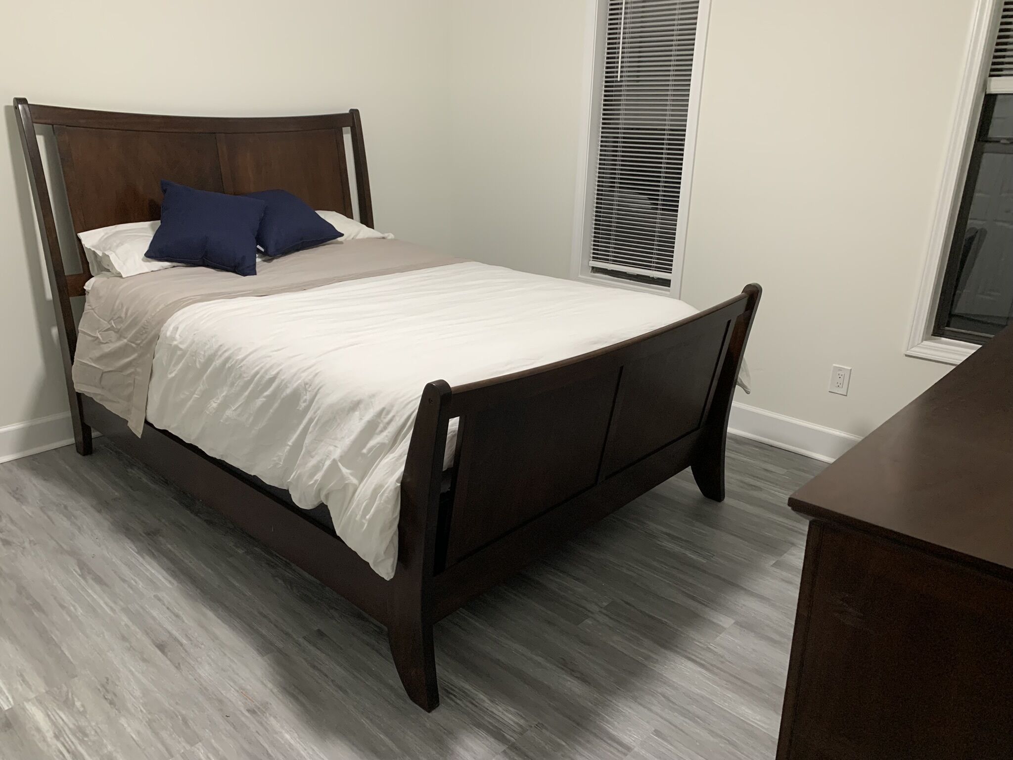 Een slaapkamer met een houten bed, wit beddengoed en een raam met jaloezieën.