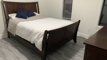 Een slaapkamer met een houten bed, wit beddengoed en een raam met jaloezieën.