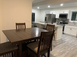 A modern kitchen with white cabinets, stainless steel appliances, and a dining area with a wooden table and chairs. - 5BR & 4BA vacation home to relax, recreate or reset, and strategically located (Roswell)