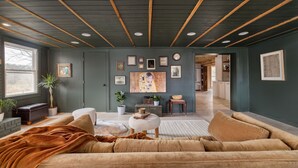 Ein gemütliches Wohnzimmer mit einer großen Couch, einem Couchtisch und einem Kamin. Mehrere gerahmte Bilder schmücken die Wand, und ein Fenster lässt natürliches Licht herein.