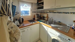 A compact kitchen with a window, a dishwasher, a stove, and a sink.