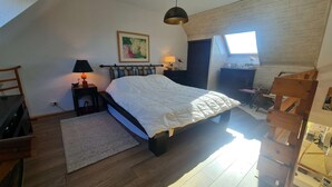 A bedroom with a large bed, a desk, a chair, a lamp, and a window.