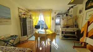 A cozy dining area with a table and chairs, a wooden cabinet, and a view of the outside through a window with yellow curtains.