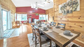 Un coin repas avec une table en bois dressée pour quatre personnes, entourée de chaises, dans une pièce aux murs en bois et dont un mur est peint en rouge.