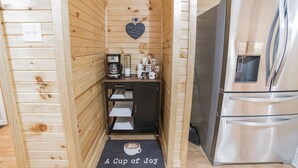 Une cuisine compacte aux murs en bois, dotée d’un réfrigérateur en acier inoxydable, d’un coin café et d’un petit placard.