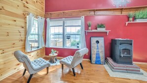 Une pièce chaleureuse avec des murs en bois, un mur d’accent rouge, une cheminée et deux fauteuils.