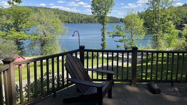 Eine Holzterrasse mit einer Bank bietet Blick auf einen See, umgeben von Bäumen und einem klaren Himmel.