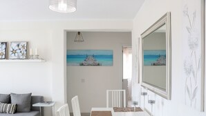 Ruokailutila, jossa on valkoinen pöytä, tuolit ja maalaus, jossa on kuvattuna laituri.
