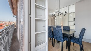 Un área de comedor con una mesa, sillas, un espejo grande y vistas de la ciudad desde un balcón.