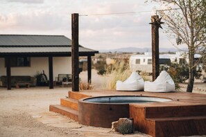 A wooden deck with a hot tub, white bean bag chairs, and a rustic house in the background. - Moon Shadow Ranch ★  Desert Medicine Retreat (Twentynine Palms)