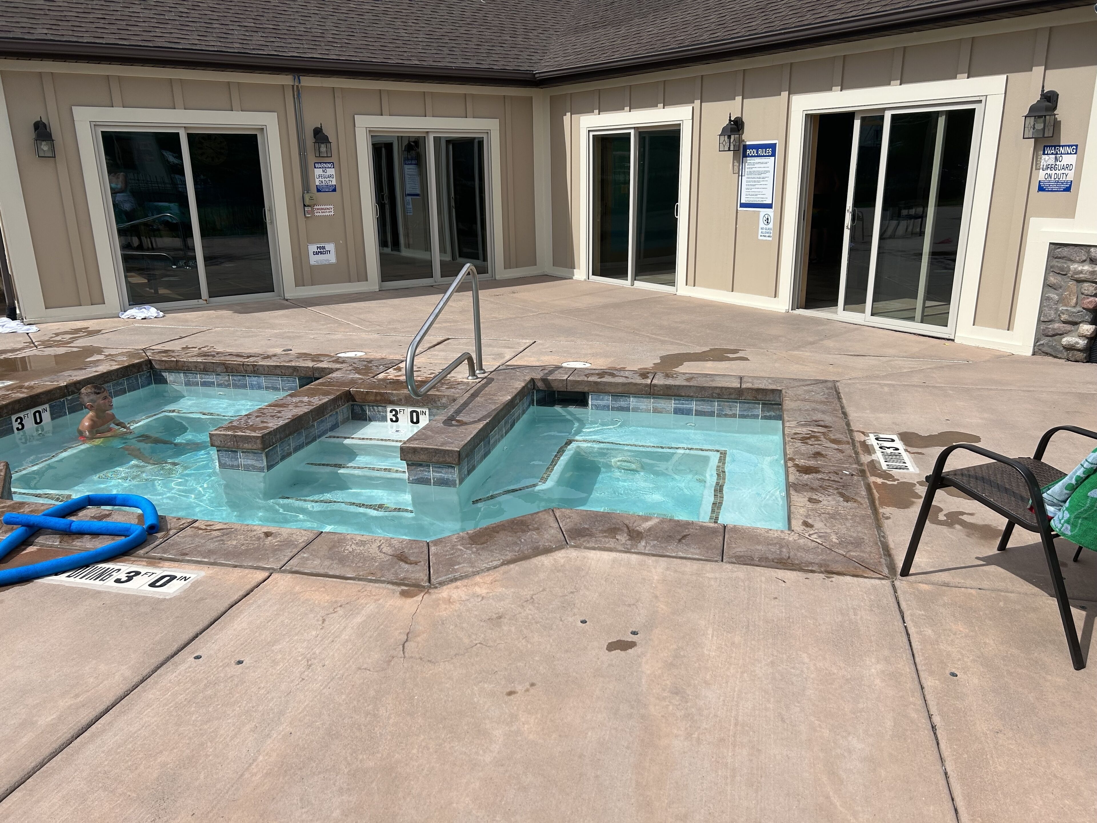 A pool area with a diving board and a lifeguard on duty sign.