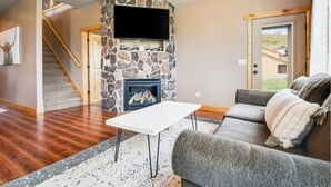 Ein Wohnzimmer mit Kamin aus Stein, einem Flachbildfernseher, einer Couch und einer Treppe.