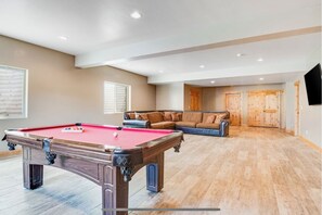 A spacious room with a pool table, a leather sofa, and wooden doors.