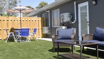 Un patio con una mesa y sillas, un sofá de mimbre y un equipo de aire acondicionado instalado en la pared.