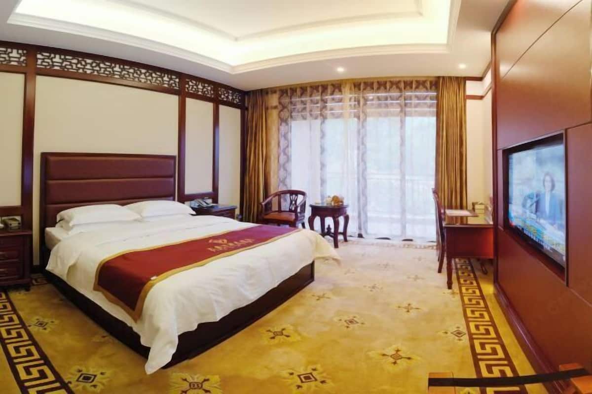 Una habitación de hotel con una cama grande, televisión, escritorio y una silla.