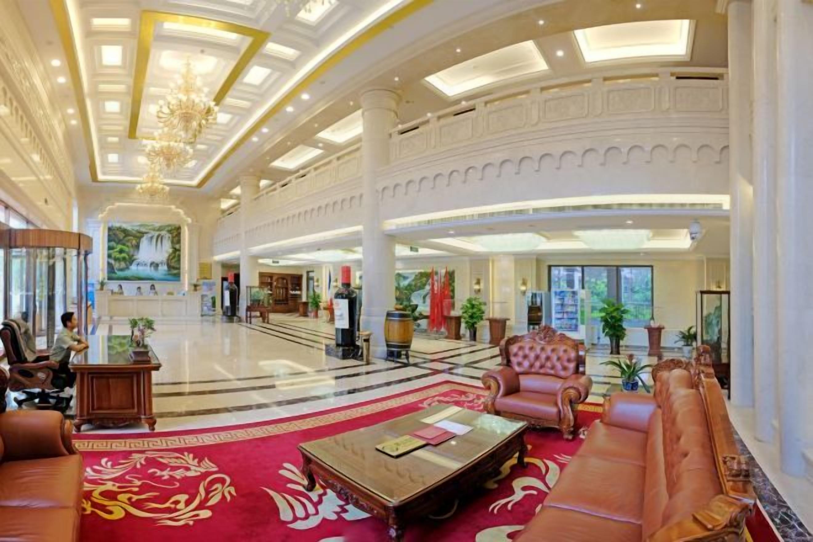 A spacious lobby with a grand chandelier, a red carpet, and a seating area with a coffee table.