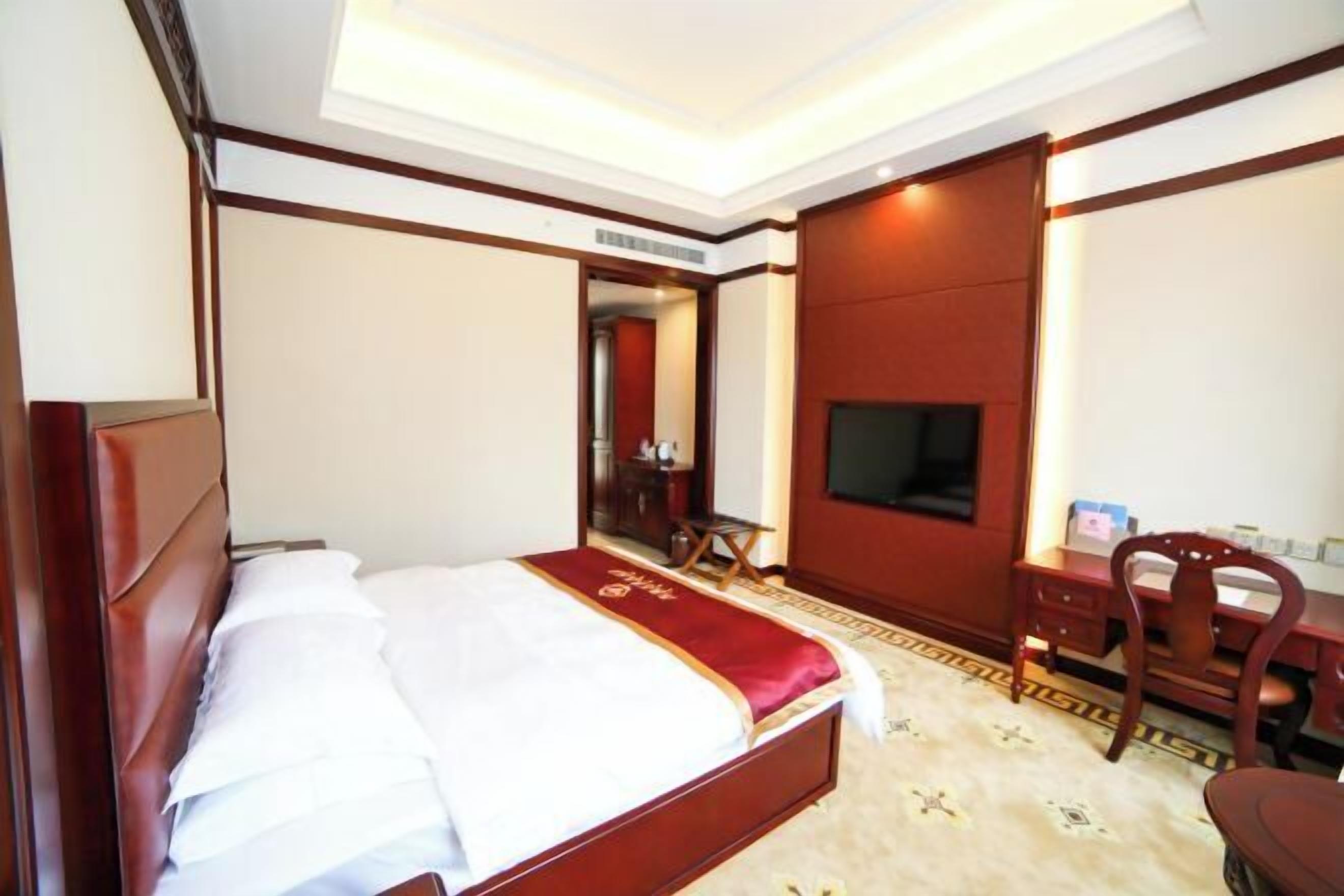 A hotel room with a bed, a desk, a chair, a television, and a mirror.