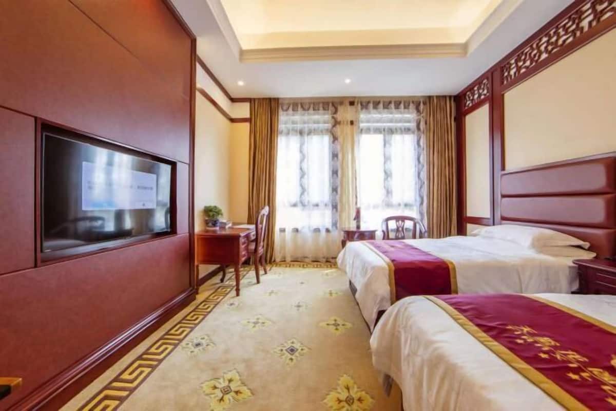 Una habitación de hotel con televisor, dos camas, un escritorio y una silla.