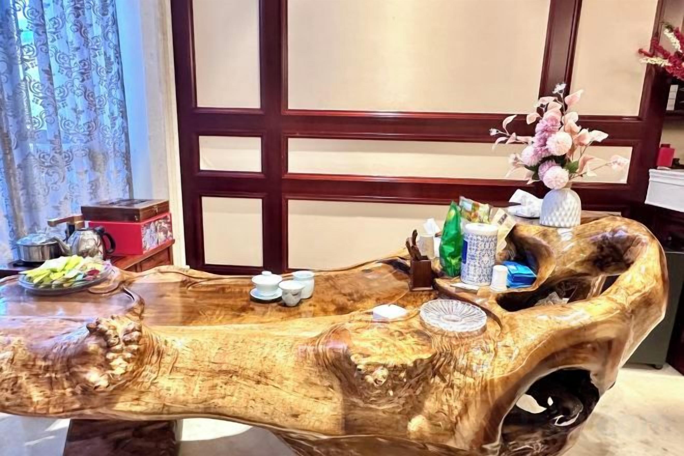Una mesa de madera con un diseño original, un florero con flores y una tetera pequeña.
