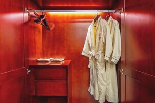 Una habitación de madera con una puerta roja, una mesita con una toalla y dos albornoces colgados en ganchos.