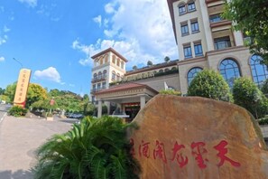 Un hotel con una entrada destacada, una gran piedra con caracteres chinos y un edificio de varios pisos y ventanas.
